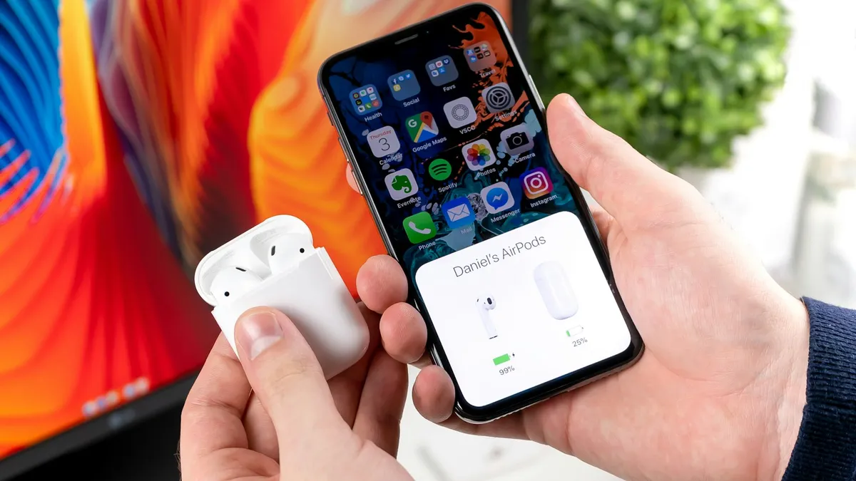 Hands holding an open AirPods case next to an iPhone that shows battery levels