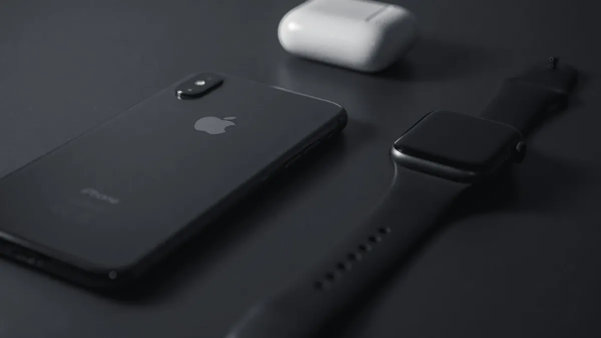 An iPhone, an Apple Watch and an AirPods case on a dark table