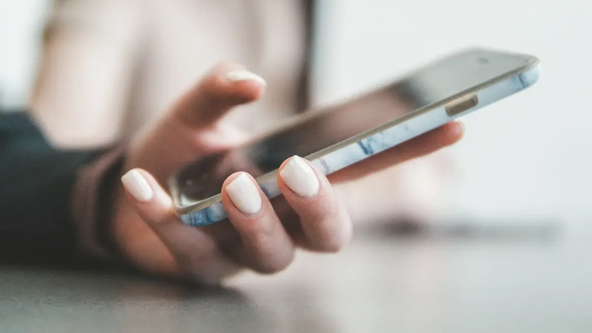 A person holding a smartphone with a marble pattern case in a bright room