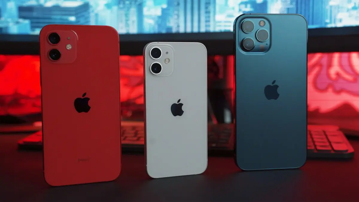 Three smartphones in red, white, and blue on a desk with a computer monitor