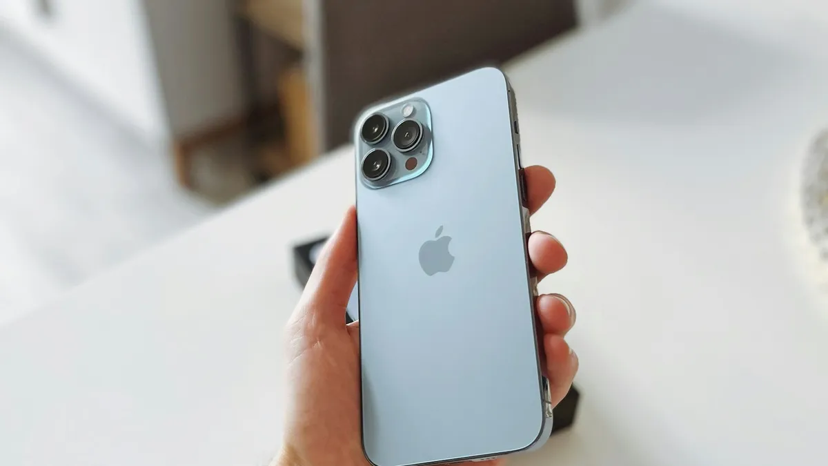 A hand holding a light blue iPhone against a white background