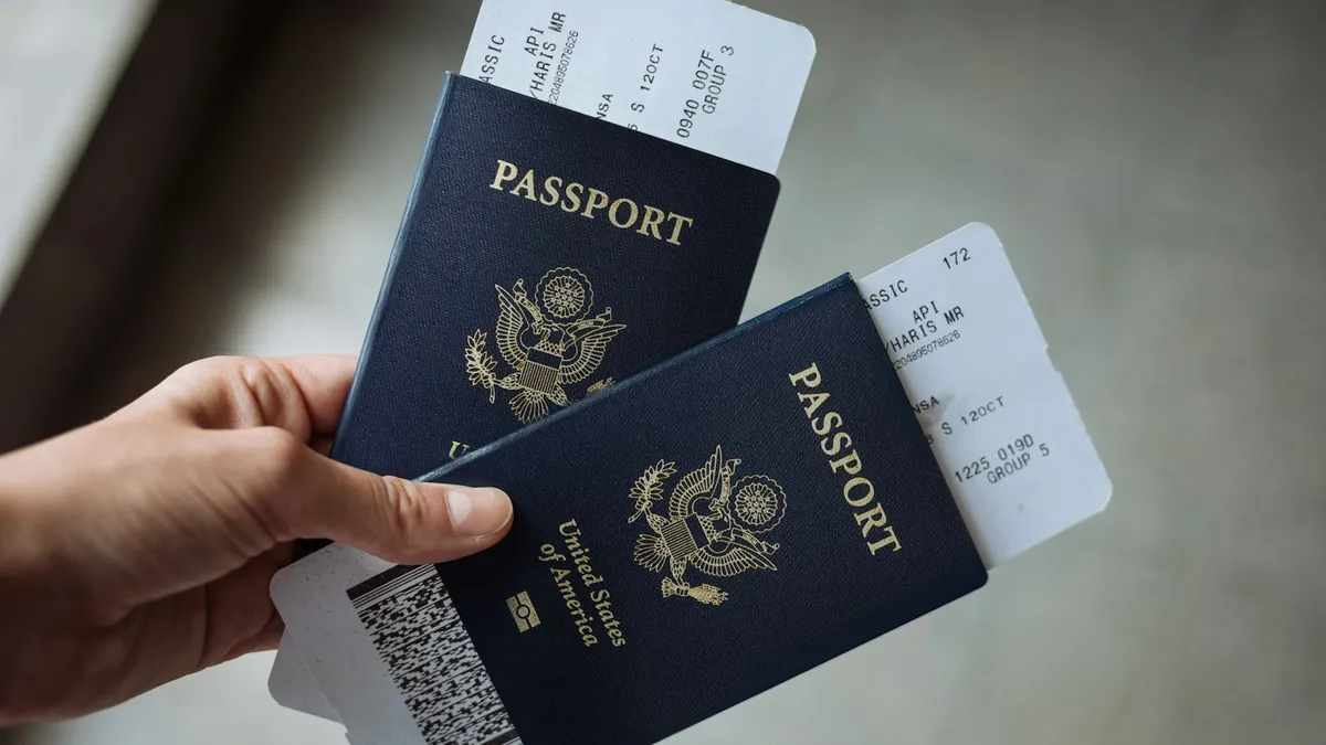 A hand holding two U.S. passports with paper boarding passes tucked inside